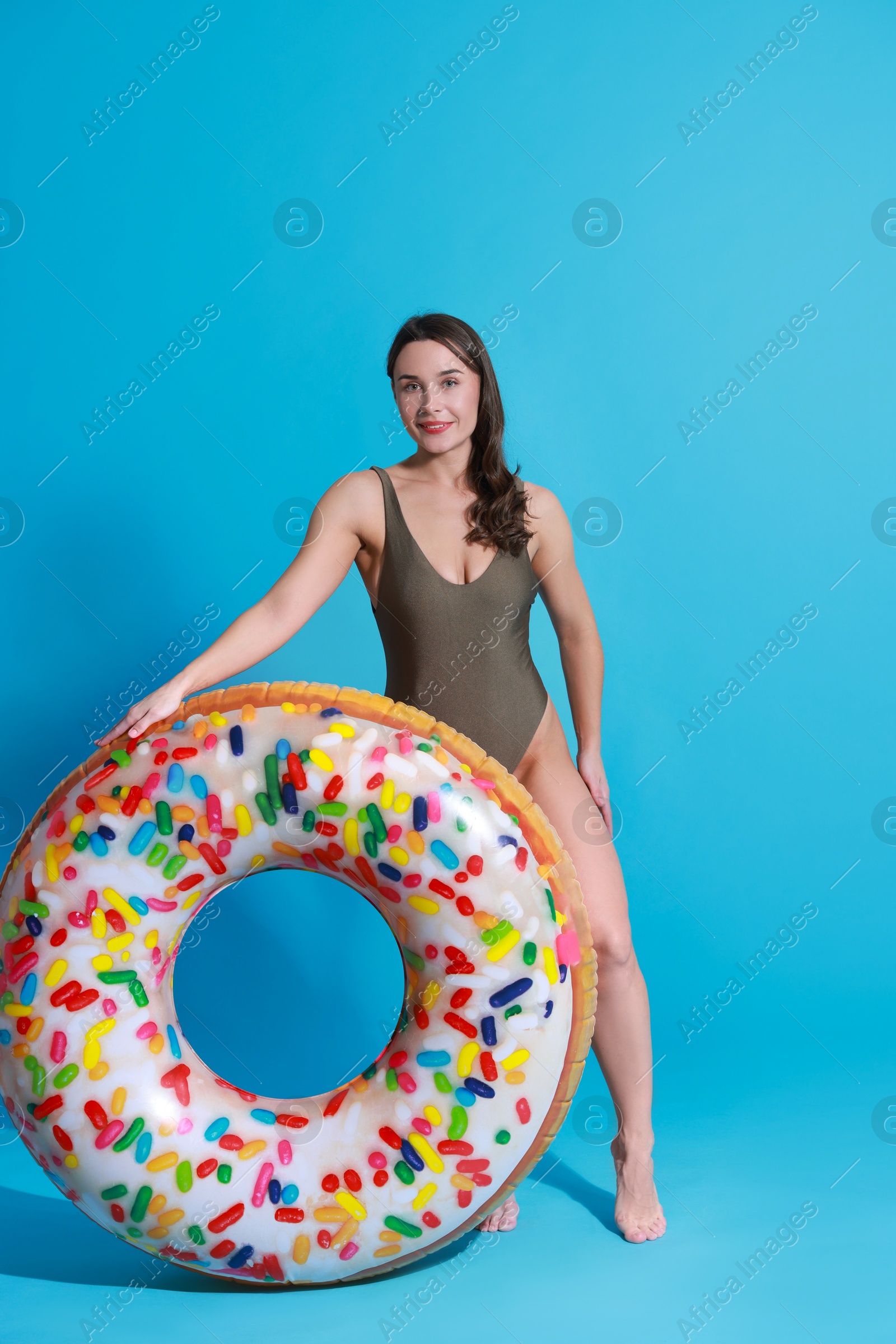 Photo of Beautiful woman in swimsuit with inflatable ring on light blue background