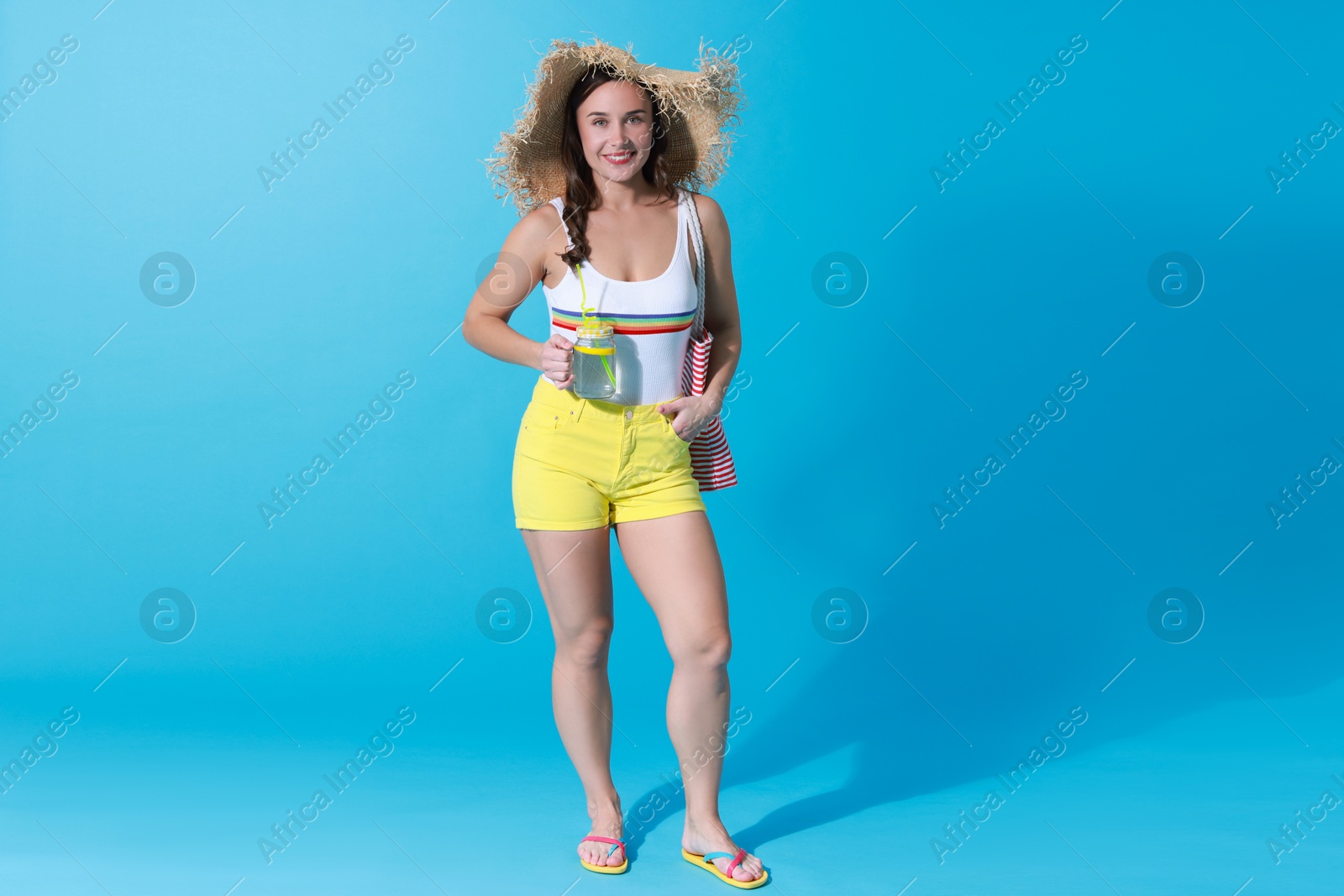 Photo of Beautiful woman in swimsuit with drink on light blue background