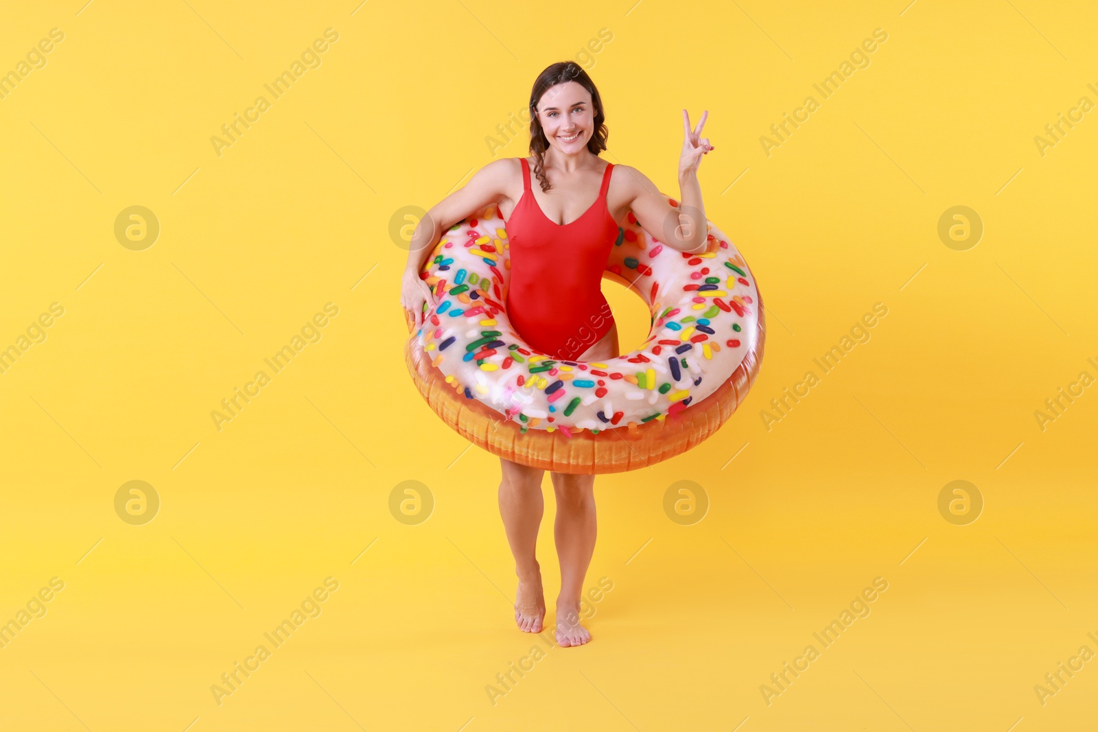 Photo of Beautiful woman in swimsuit with inflatable ring on yellow background