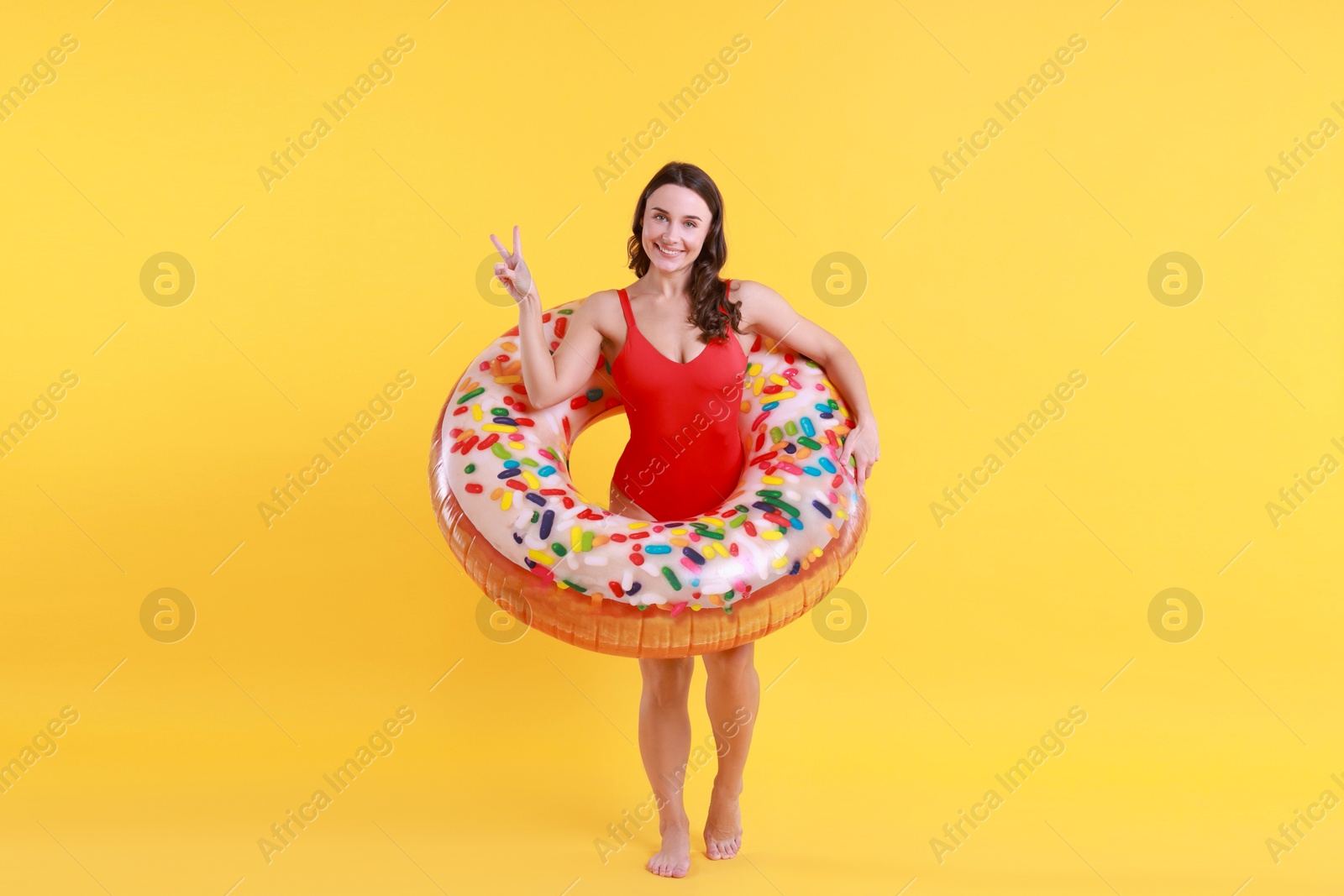 Photo of Beautiful woman in swimsuit with inflatable ring on yellow background