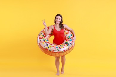 Photo of Beautiful woman in swimsuit with inflatable ring on yellow background