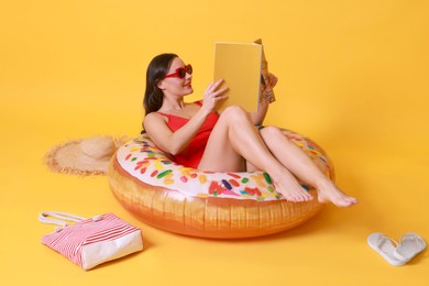 Photo of Beautiful woman with beach accessories reading magazine on yellow background