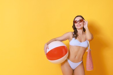 Photo of Beautiful woman in swimsuit with inflatable ball on yellow background. Space for text