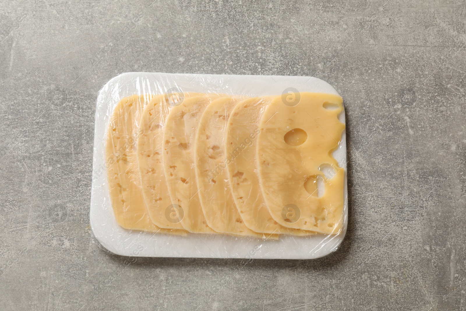 Photo of Pack of sliced cheese on grey table, top view