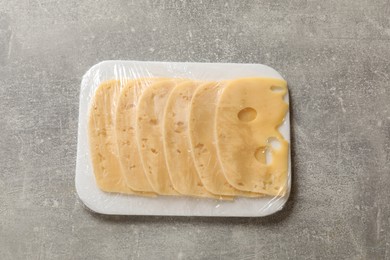 Photo of Pack of sliced cheese on grey table, top view