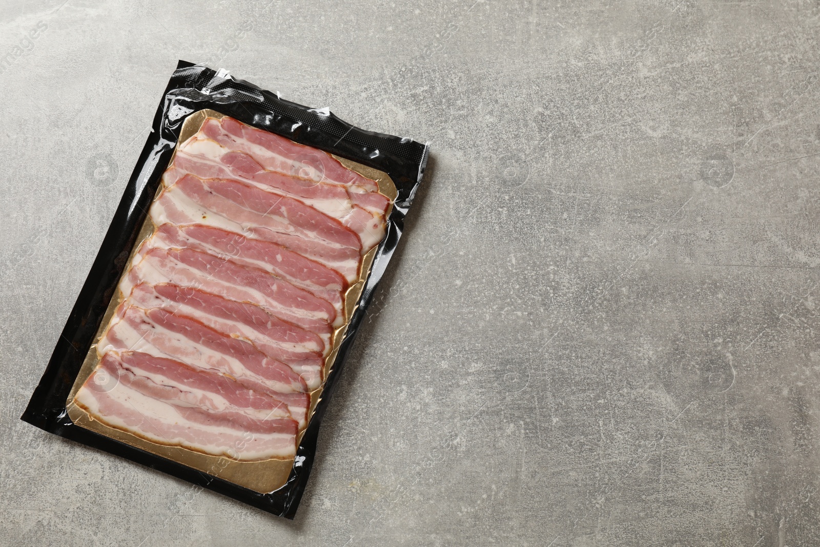 Photo of Pack of sliced bacon on grey table, top view. Space for text