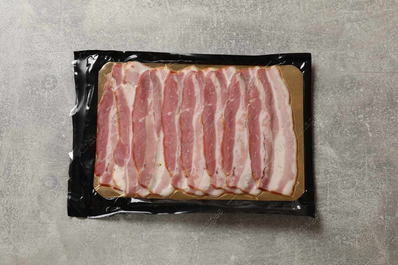 Photo of Pack of sliced bacon on grey table, top view