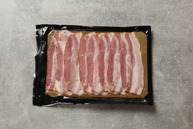 Photo of Pack of sliced bacon on grey table, top view