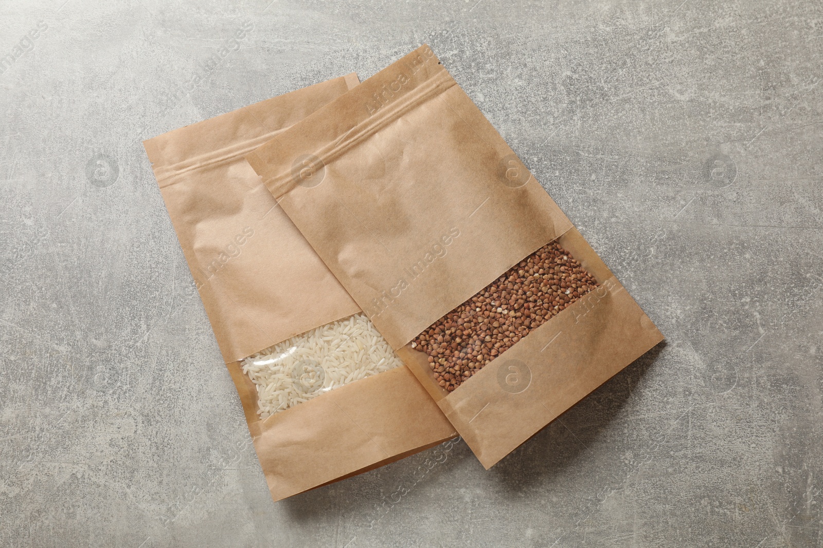 Photo of Paper pouch bags with buckwheat and rice on grey table, top view