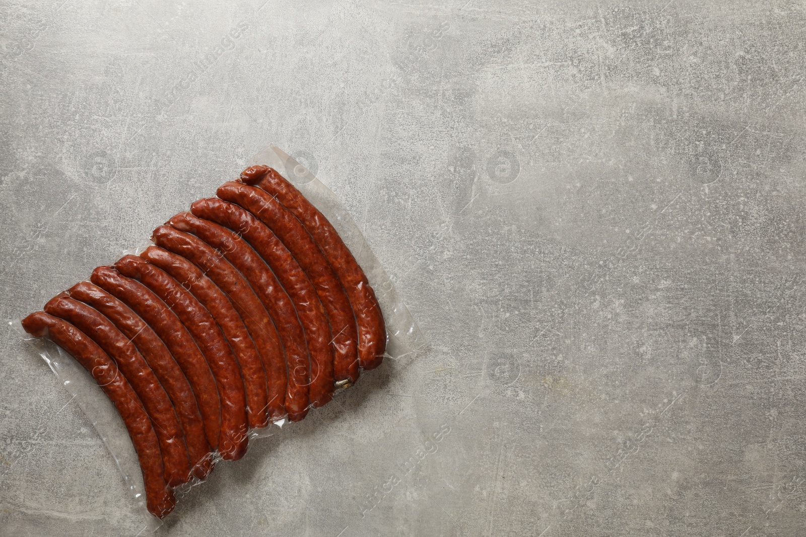 Photo of Pack of dry smoked sausages on grey table, top view. Space for text