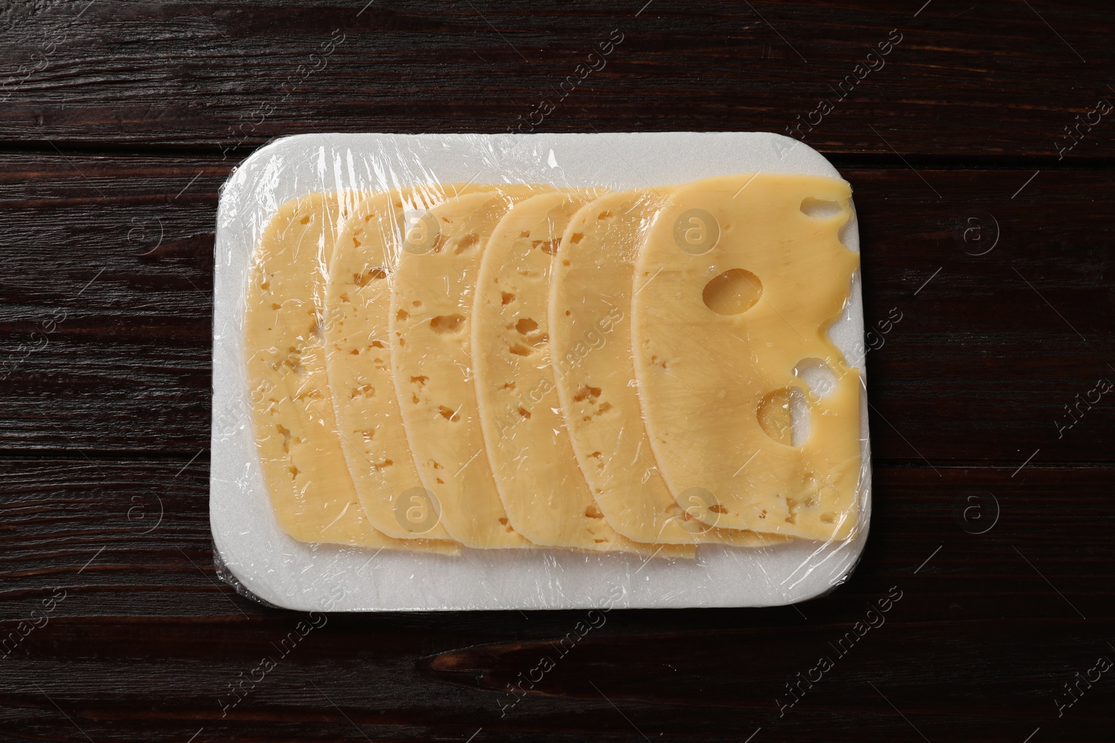 Photo of Pack of sliced cheese on wooden table, top view