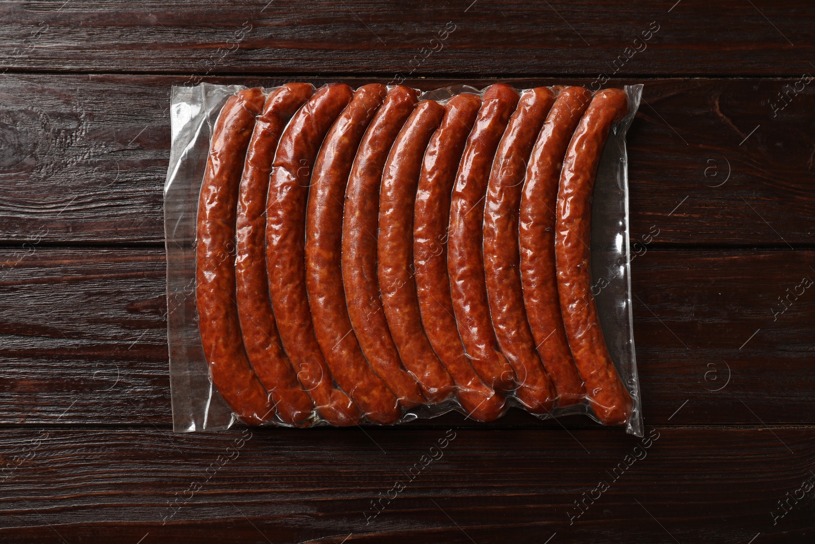 Photo of Pack of dry smoked sausages on wooden table, top view