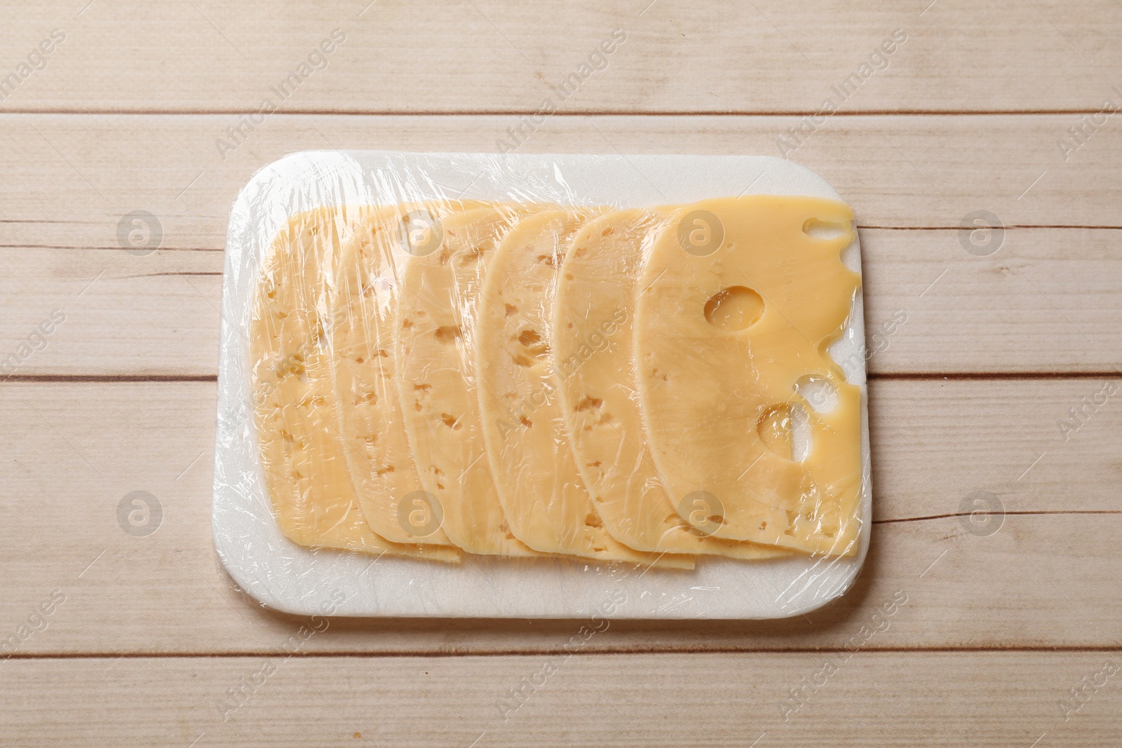 Photo of Pack of sliced cheese on wooden table, top view