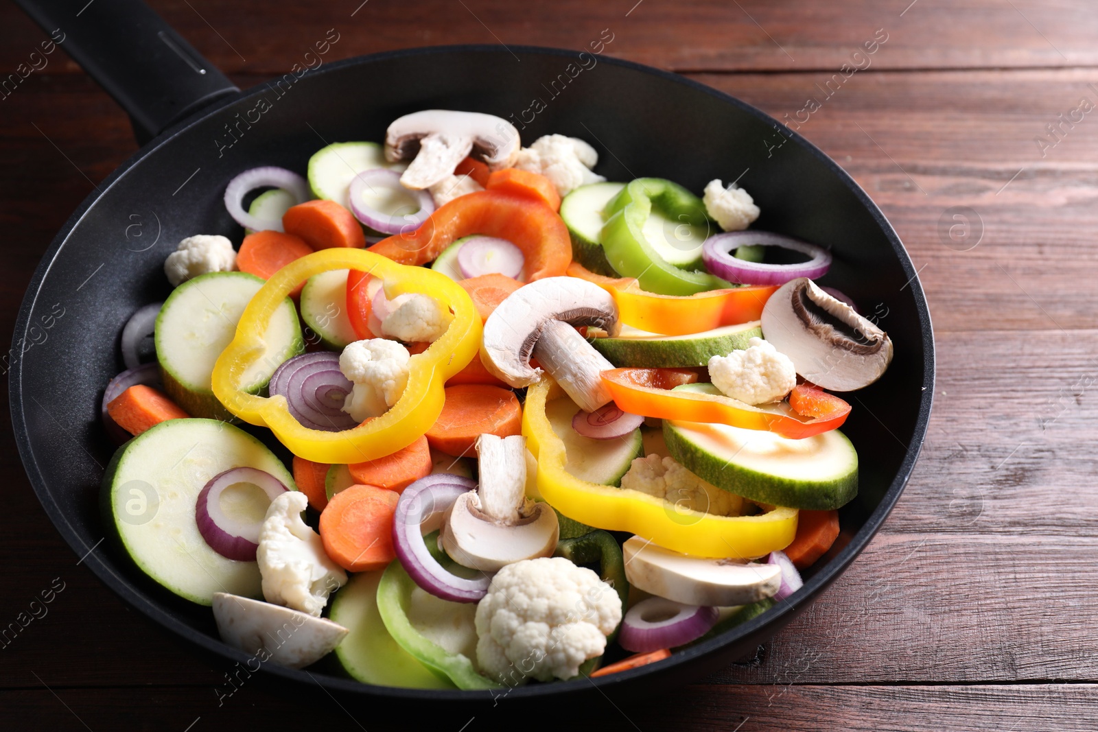 Photo of Frying pan with mix of vegetables and mushrooms on wooden table, closeup