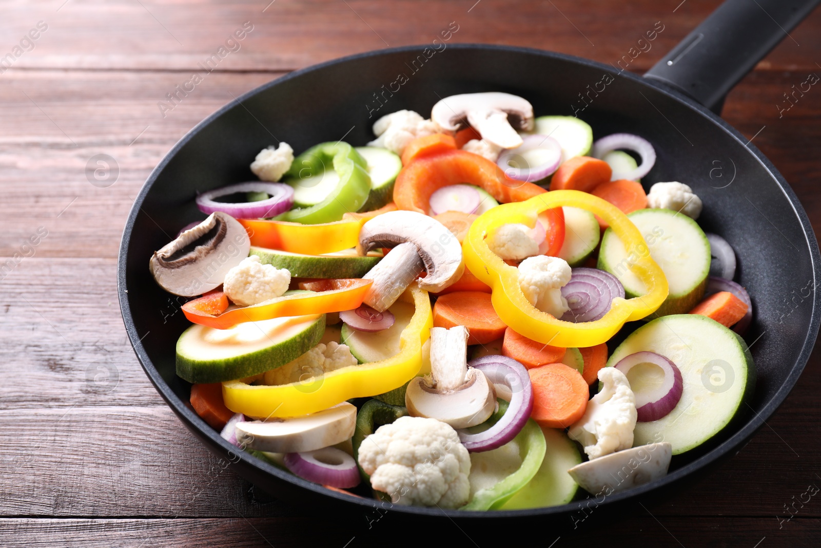 Photo of Frying pan with mix of vegetables and mushrooms on wooden table, closeup