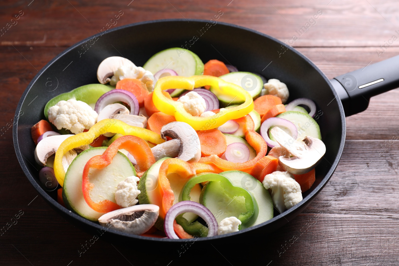 Photo of Frying pan with mix of vegetables and mushrooms on wooden table, closeup