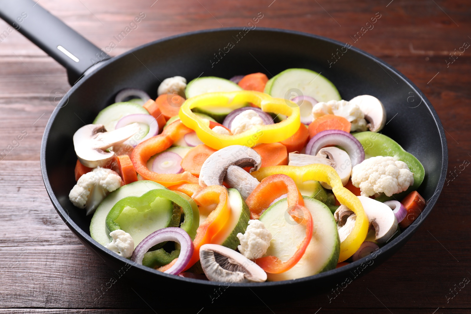 Photo of Frying pan with mix of vegetables and mushrooms on wooden table, closeup