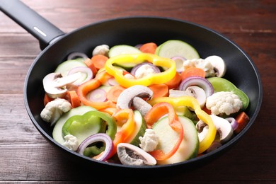 Photo of Frying pan with mix of vegetables and mushrooms on wooden table, closeup