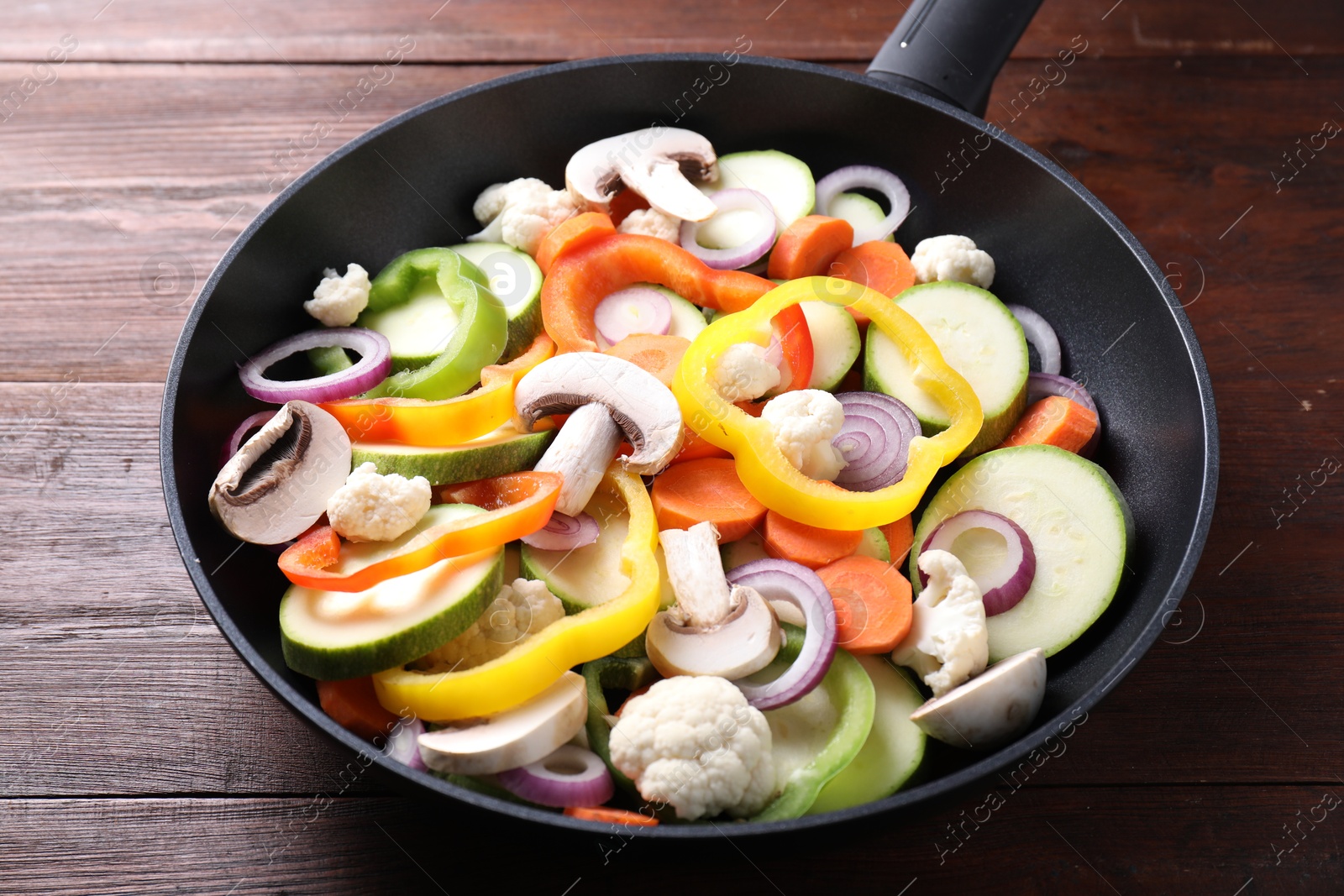 Photo of Frying pan with mix of vegetables and mushrooms on wooden table, closeup