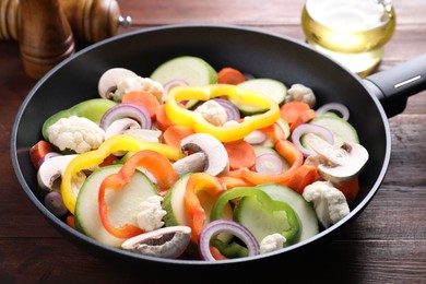 Photo of Frying pan with mix of vegetables and mushrooms on wooden table, closeup