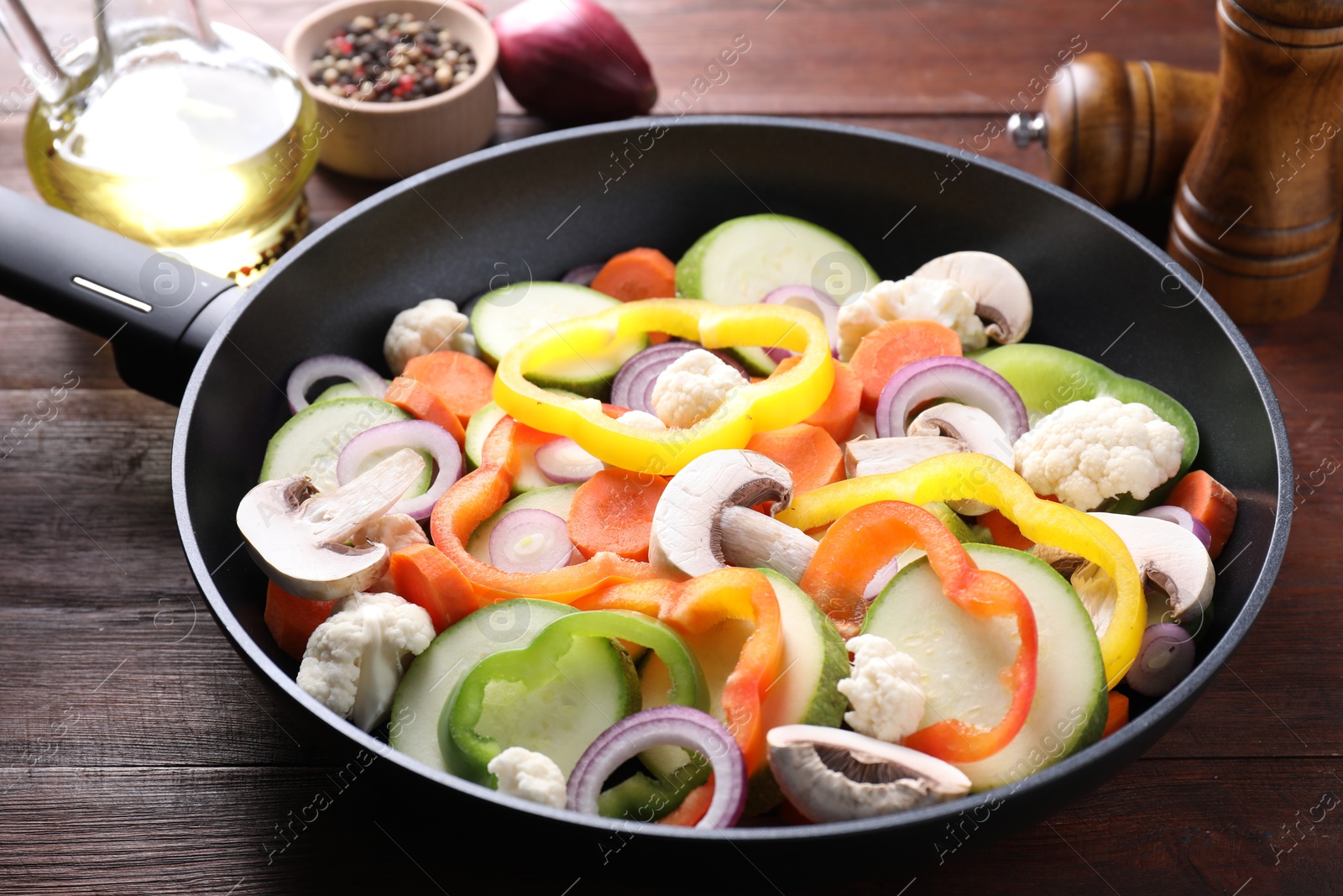 Photo of Frying pan with mix of vegetables and mushrooms on wooden table, closeup