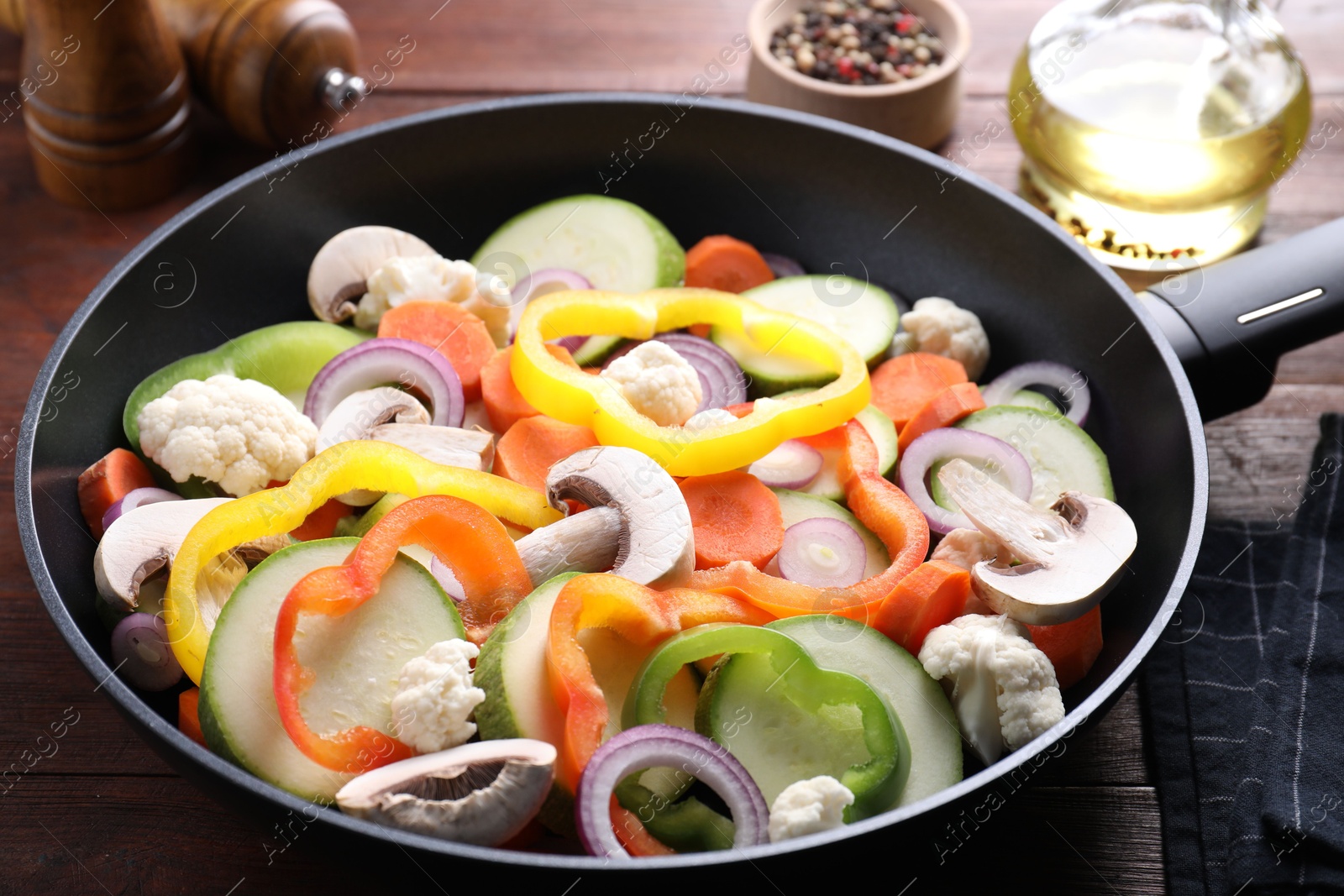 Photo of Frying pan with mix of vegetables and mushrooms on wooden table, closeup