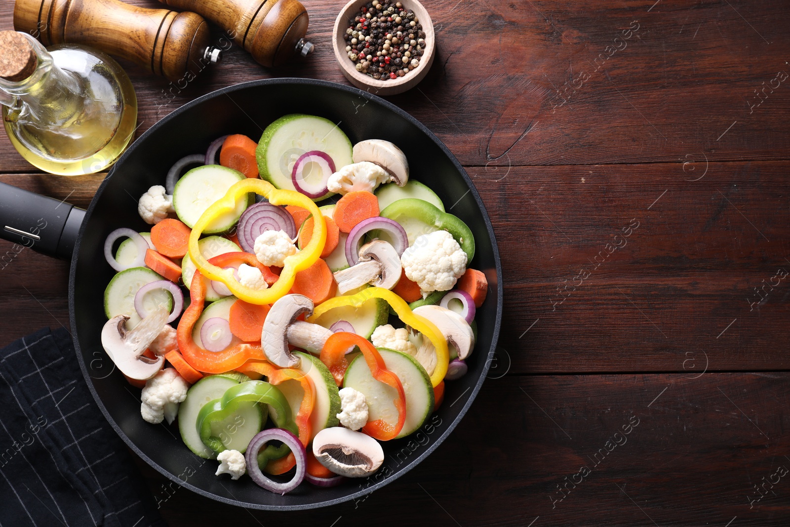 Photo of Frying pan with mix of vegetables and mushrooms on wooden table, top view. Space for text