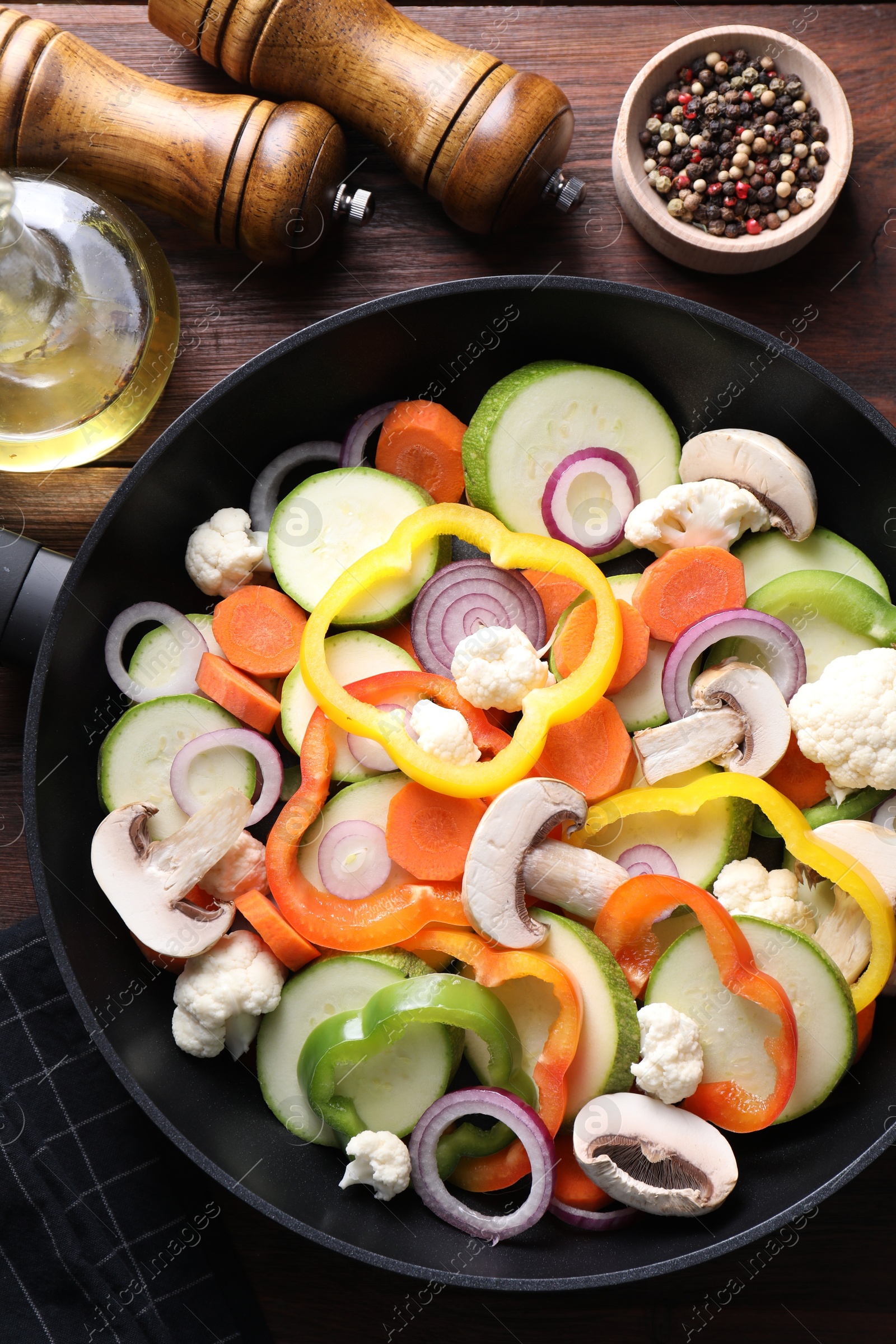 Photo of Frying pan with mix of vegetables and mushrooms on wooden table, top view