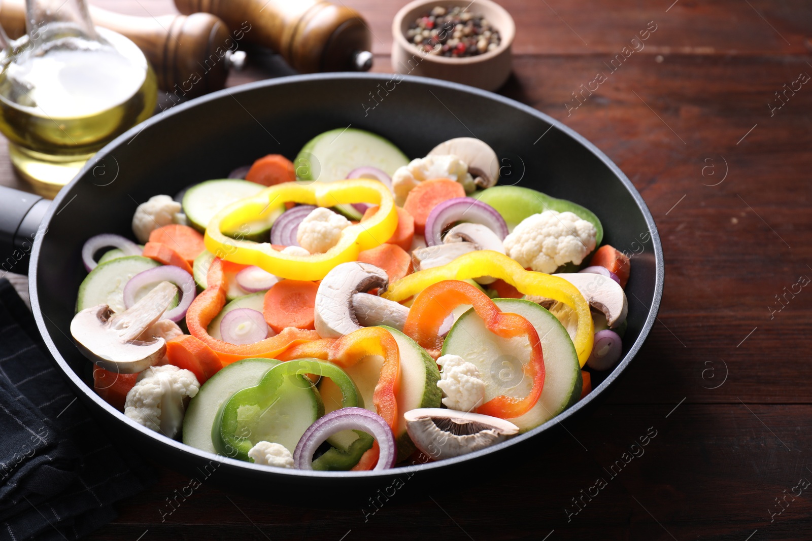 Photo of Frying pan with mix of vegetables and mushrooms on wooden table, closeup