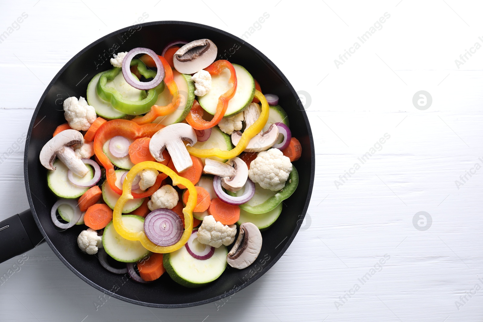 Photo of Frying pan with mix of vegetables and mushrooms on white wooden table, top view. Space for text