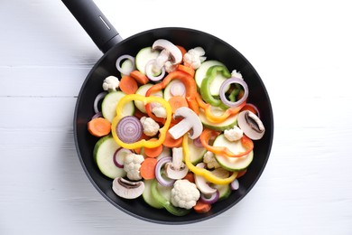 Photo of Frying pan with mix of vegetables and mushrooms on white wooden table, top view