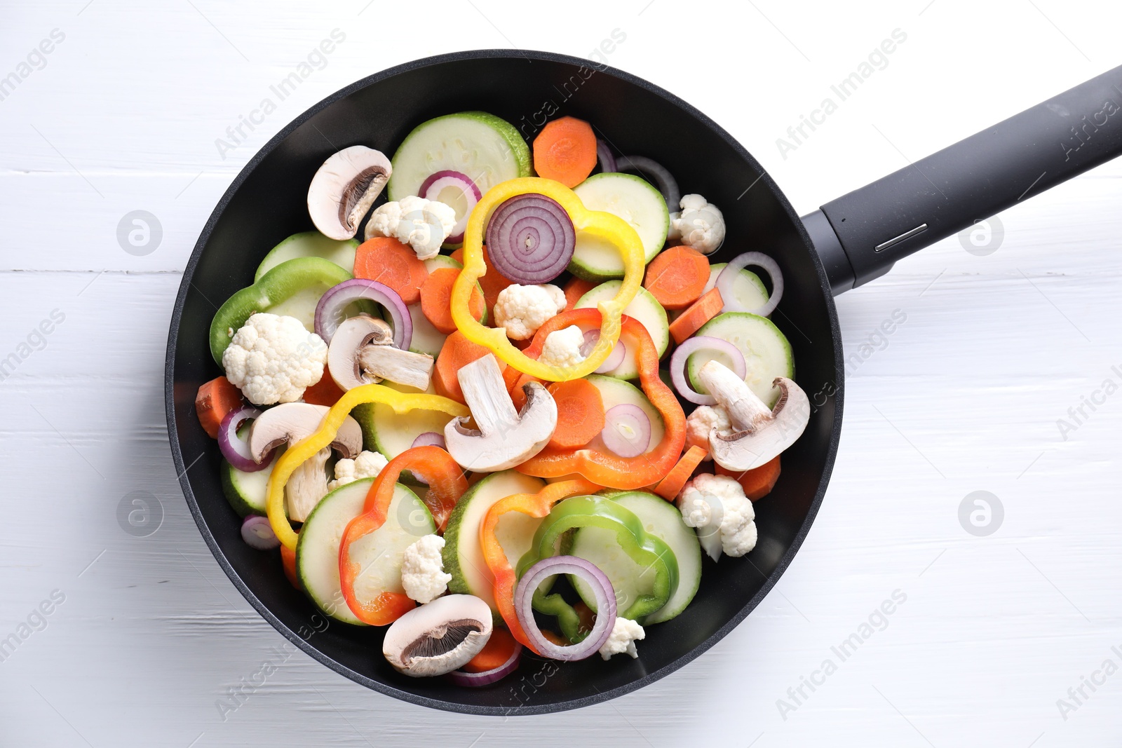 Photo of Frying pan with mix of vegetables and mushrooms on white wooden table, top view