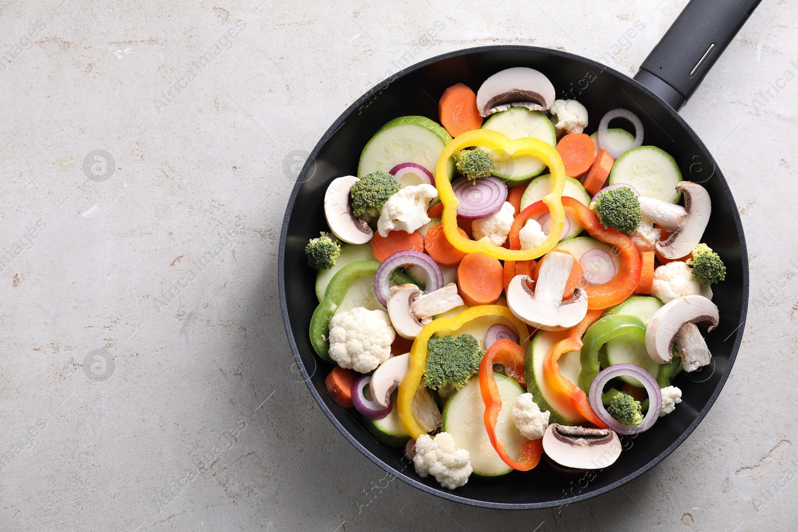 Photo of Frying pan with mix of vegetables and mushrooms on light grey table, top view. Space for text