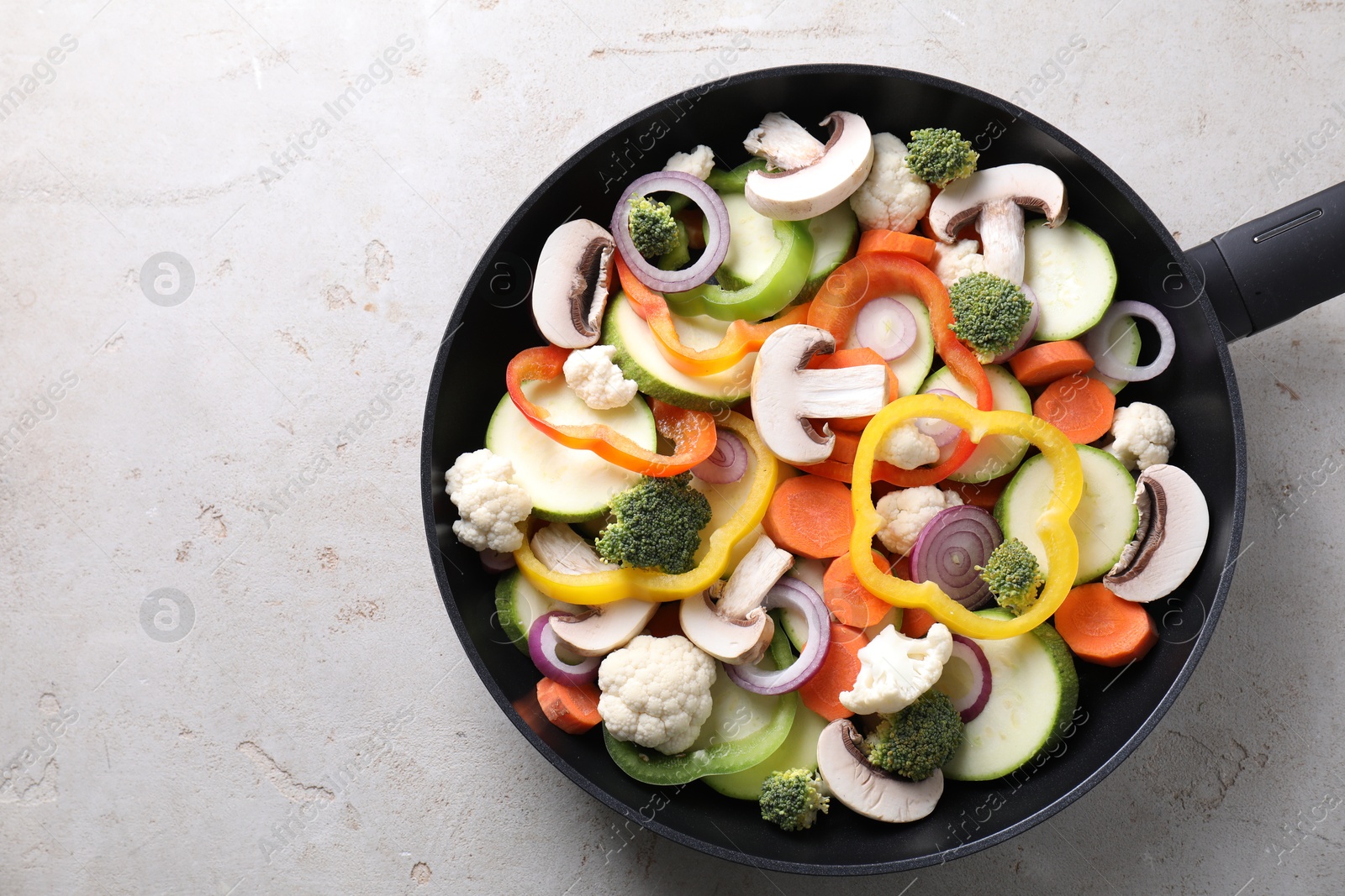 Photo of Frying pan with mix of vegetables and mushrooms on light grey table, top view. Space for text