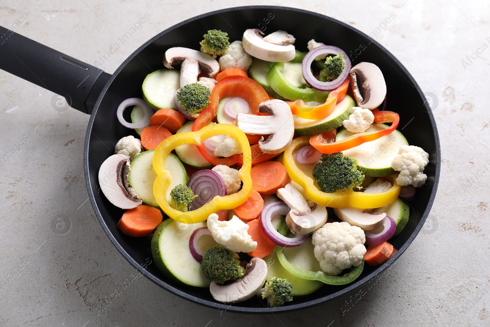 Photo of Frying pan with mix of vegetables and mushrooms on light grey table, above view