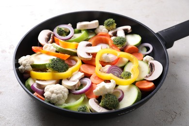 Photo of Frying pan with mix of vegetables and mushrooms on light grey table, closeup