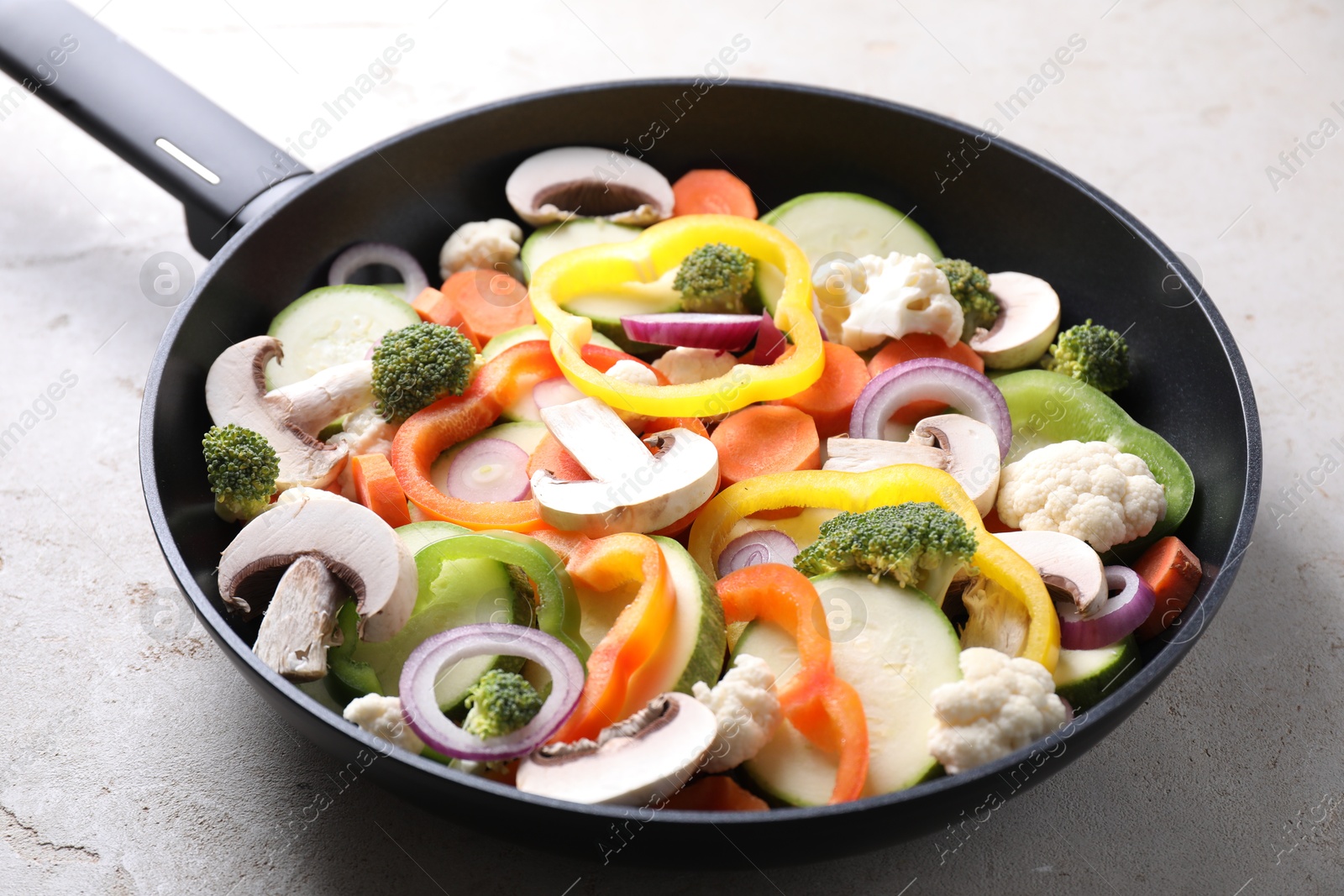 Photo of Frying pan with mix of vegetables and mushrooms on light grey table, closeup