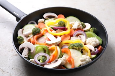 Photo of Frying pan with mix of vegetables and mushrooms on light grey table, closeup