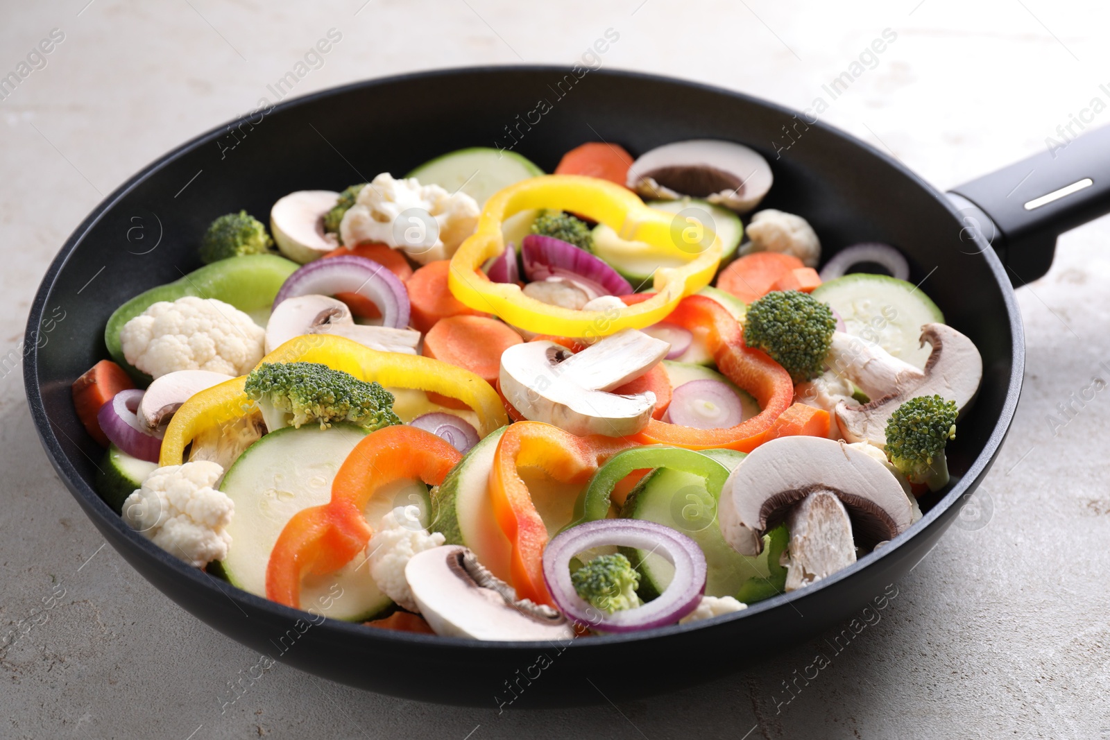 Photo of Frying pan with mix of vegetables and mushrooms on light grey table, closeup