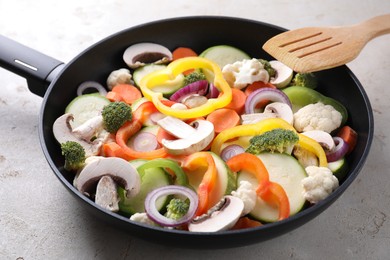 Photo of Frying pan with mix of vegetables, mushrooms and slotted turner on light grey table, closeup