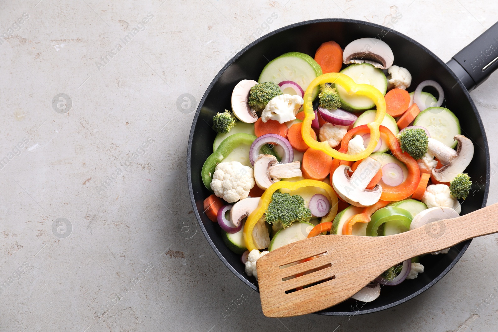 Photo of Frying pan with mix of vegetables, mushrooms and slotted turner on light grey table, top view. Space for text