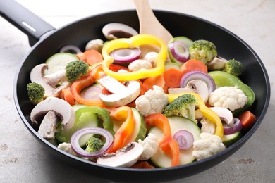 Frying pan with mix of vegetables and mushrooms on light grey table, closeup