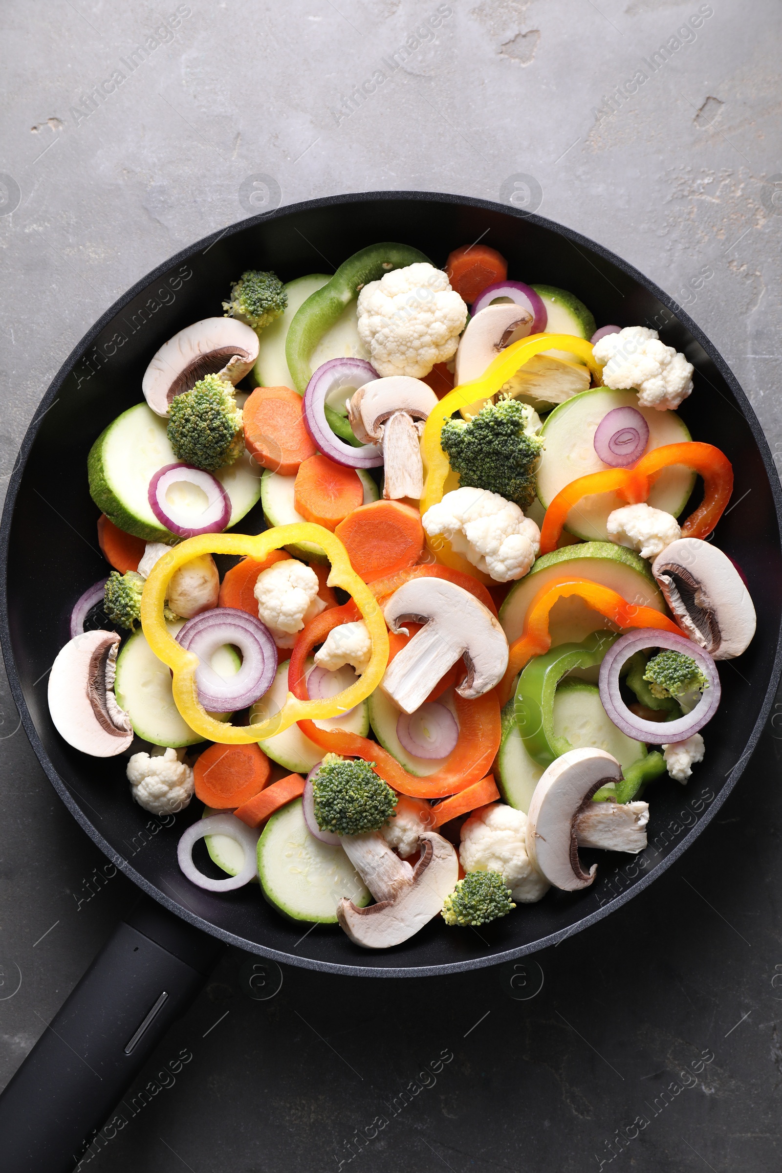 Photo of Frying pan with mix of vegetables and mushrooms on grey table, top view