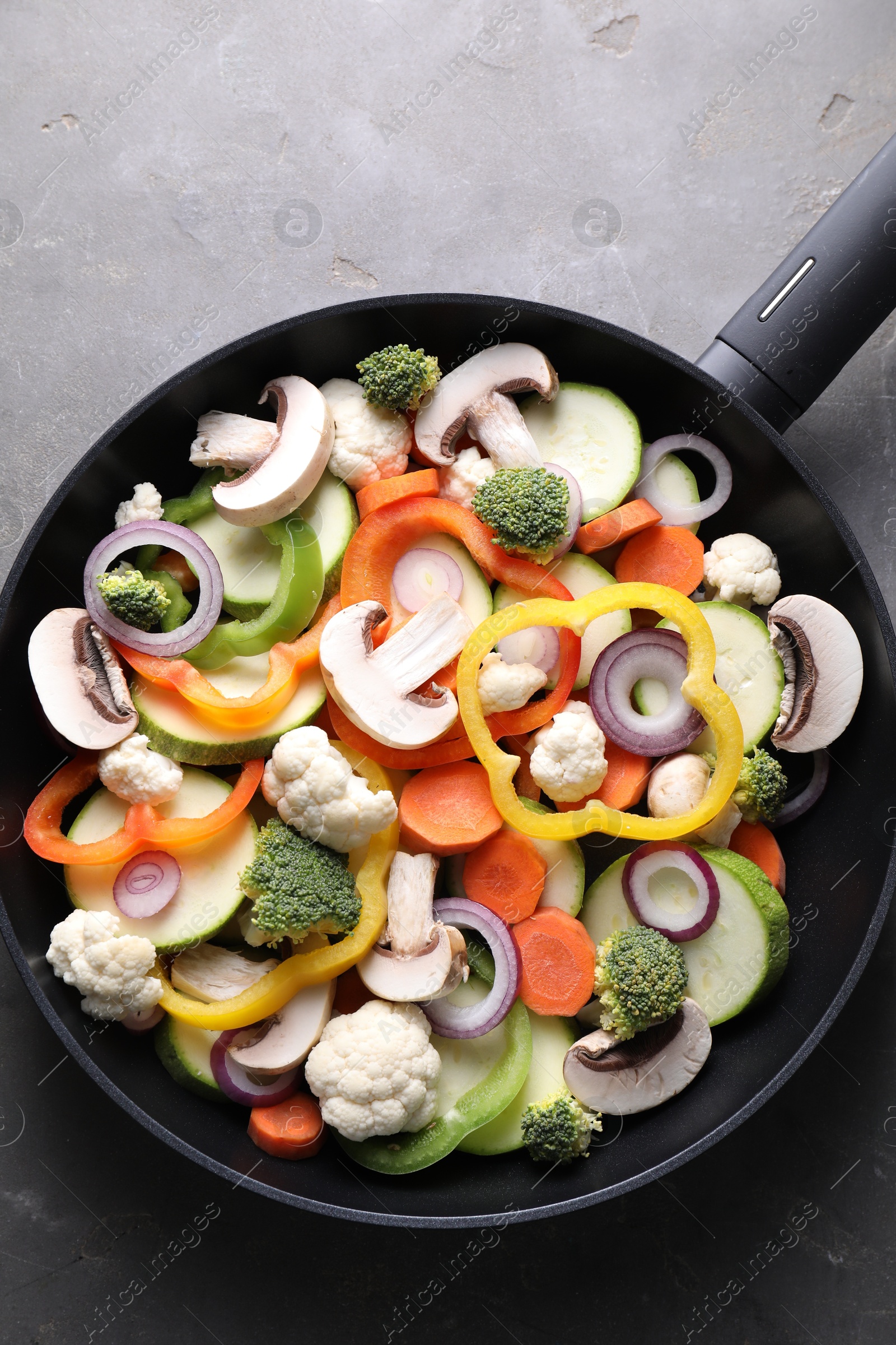 Photo of Frying pan with mix of vegetables and mushrooms on grey table, top view