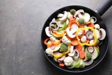 Photo of Frying pan with mix of vegetables and mushrooms on grey table, top view. Space for text