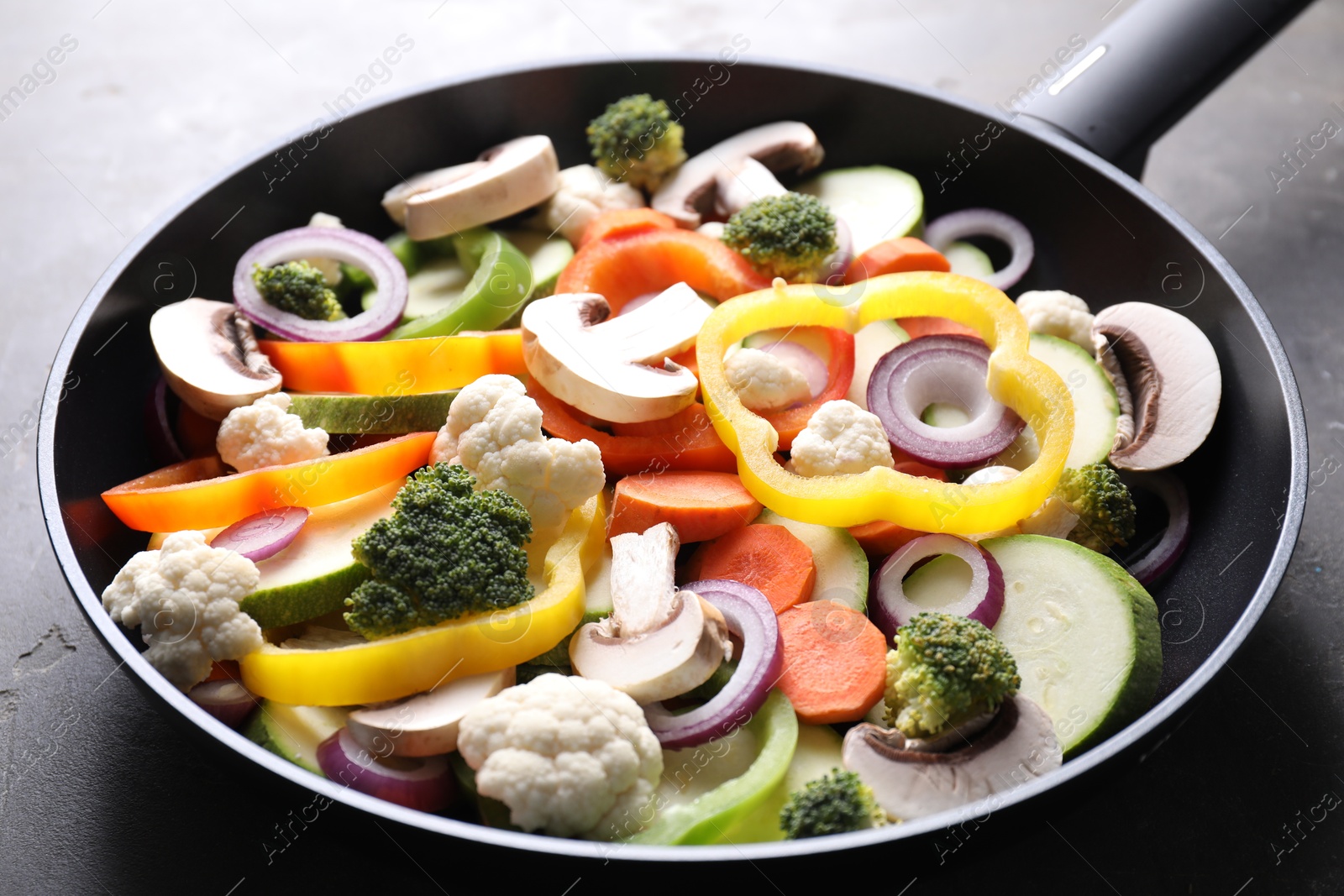 Photo of Frying pan with mix of vegetables and mushrooms on grey table, closeup