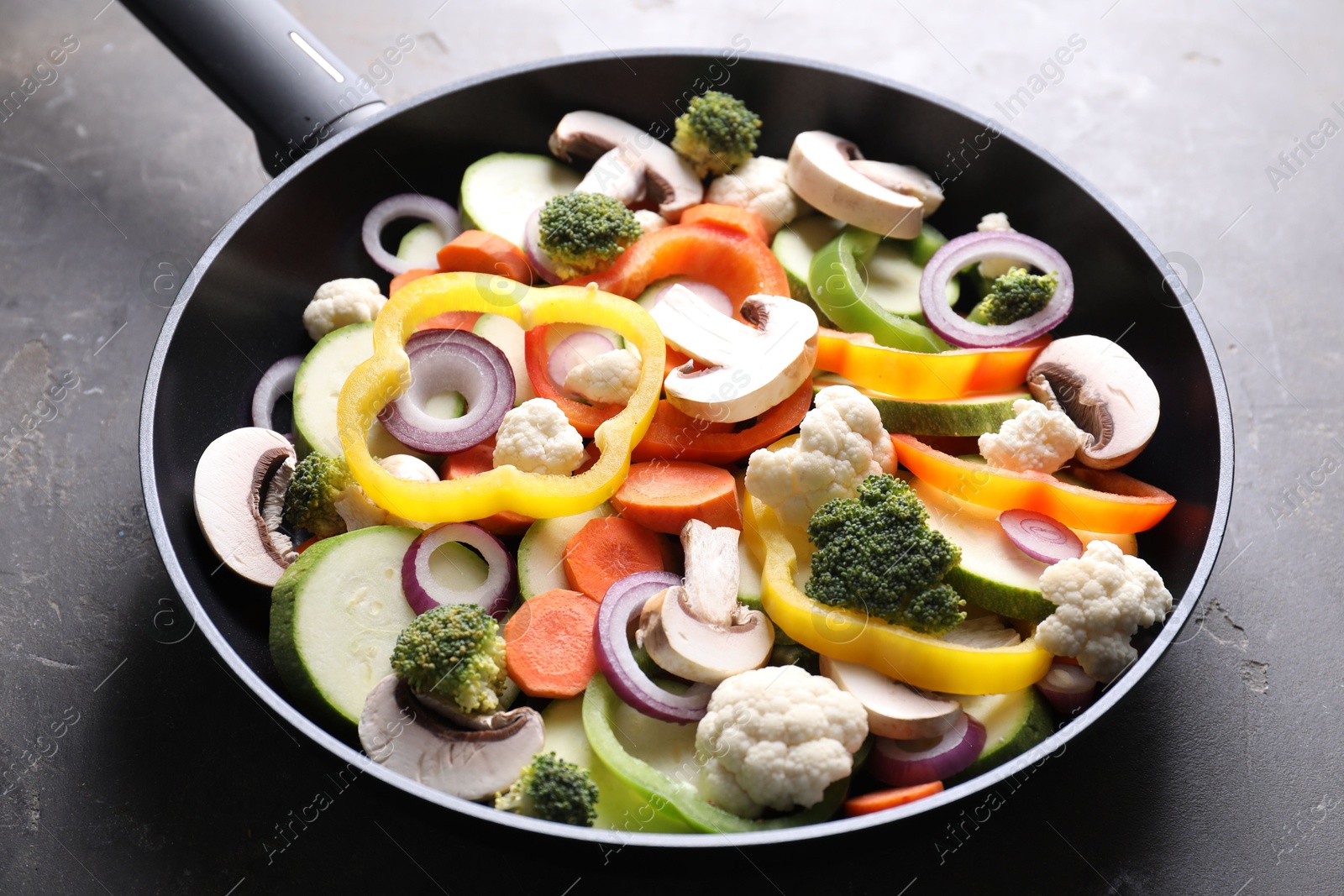 Photo of Frying pan with mix of vegetables and mushrooms on grey table, closeup