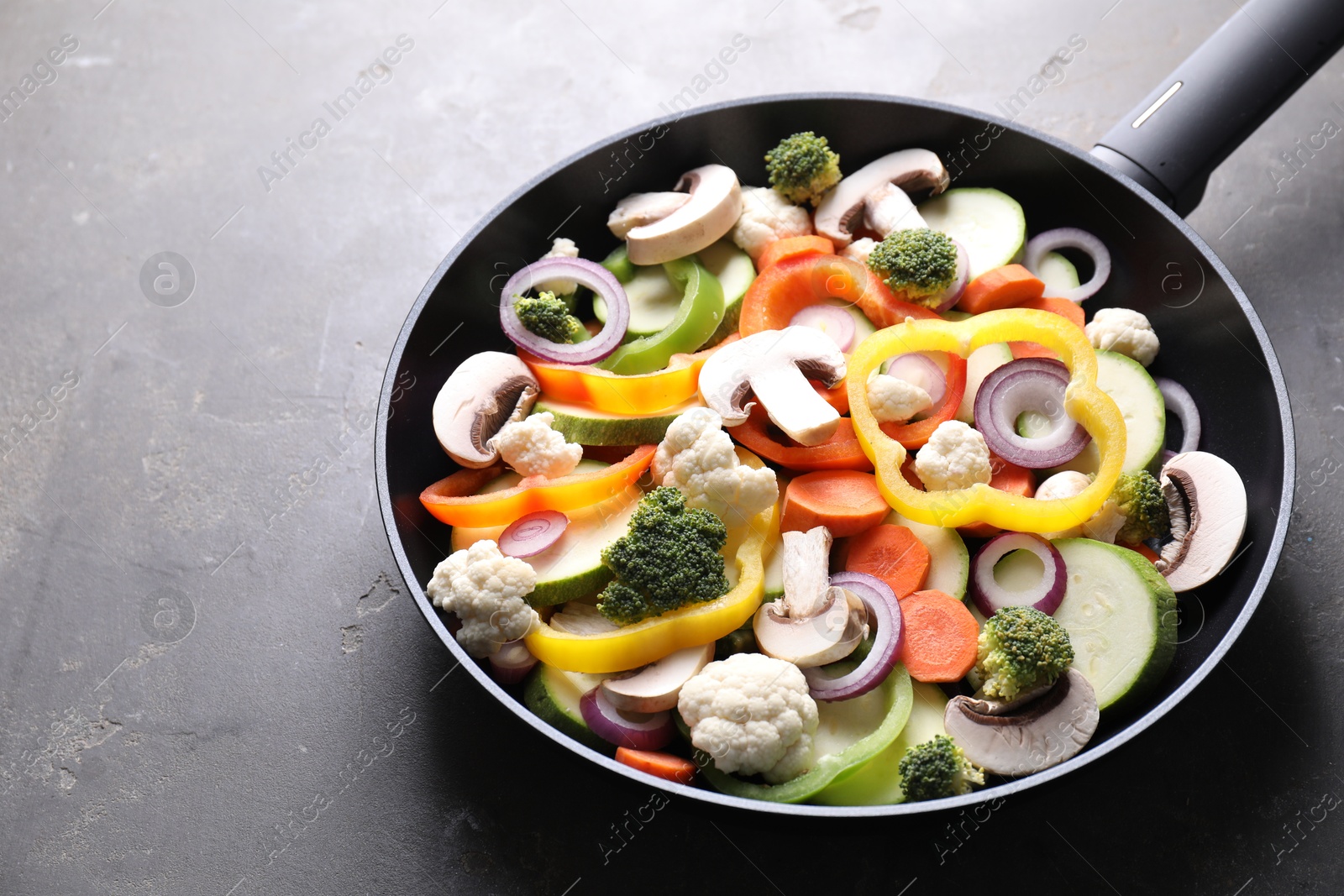 Photo of Frying pan with mix of vegetables and mushrooms on grey table, closeup. Space for text