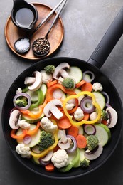 Photo of Frying pan with mix of vegetables, mushrooms and spices on grey table, top view