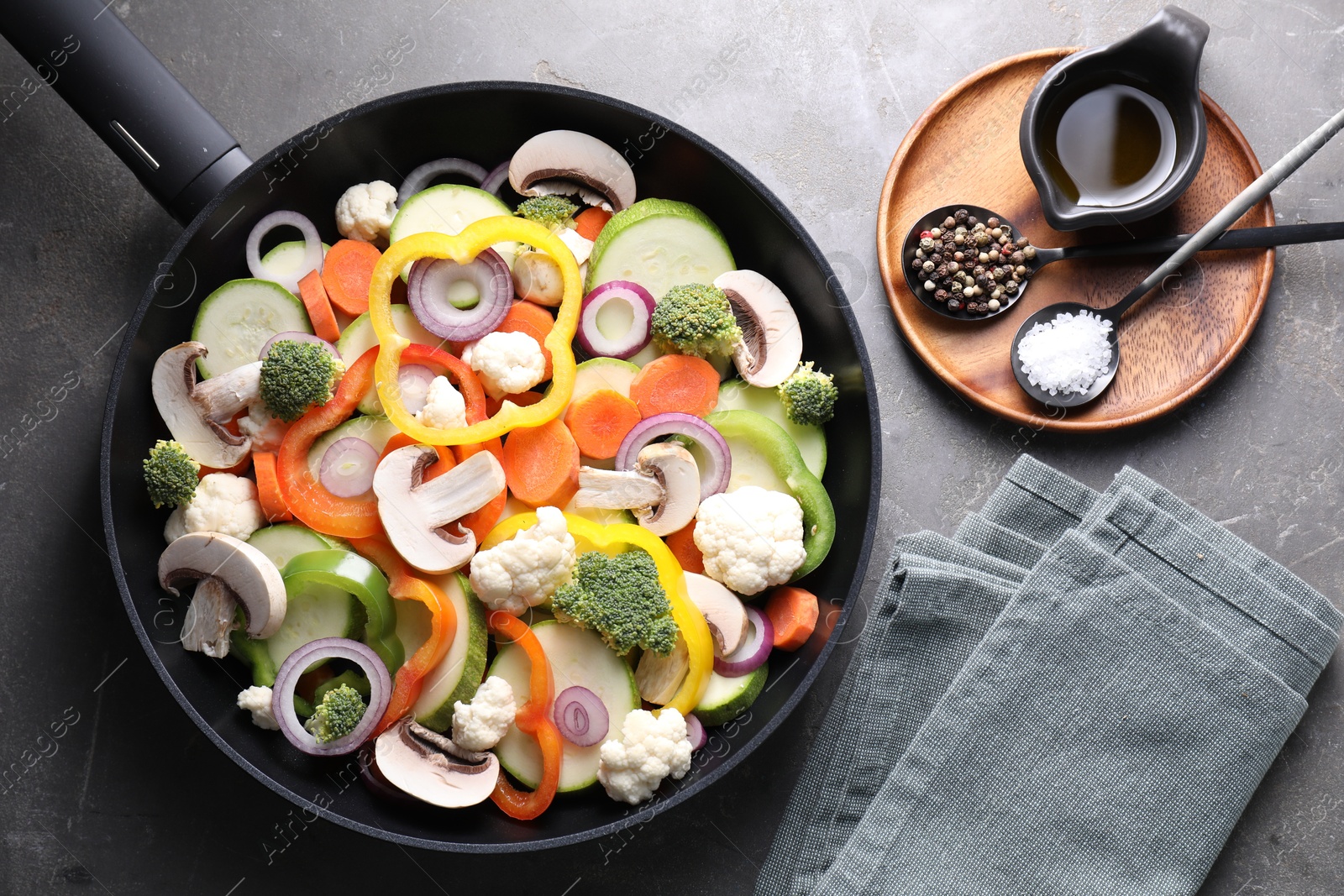 Photo of Frying pan with mix of vegetables, mushrooms and spices on grey table, top view